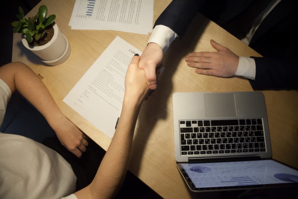 Business partners shaking hands over signed contract documents